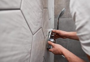 Male plumber hands installing shower faucet handle in bathroom.