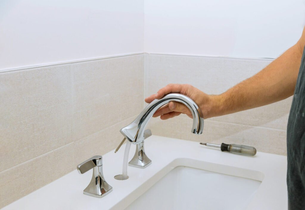 A plumber at work assembles and installs a water faucet in the bathroom of his client